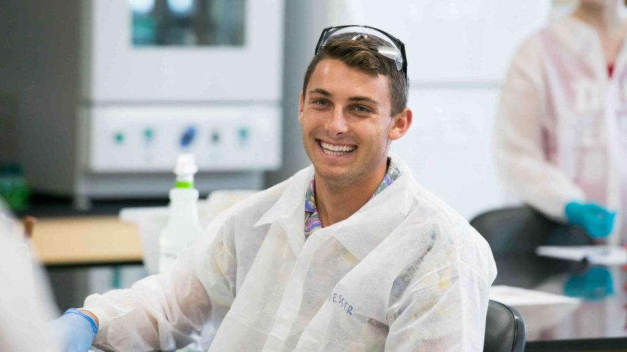 Male PLNU student in lab coat and glasses smiles