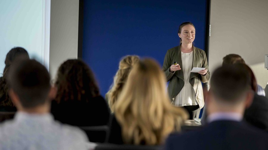 Woman presents in front of a crowded room