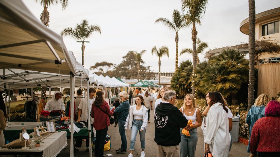PLNU students, alumni, and visitors gather around outdoor vendor booths during a Homecoming celebration on campus.