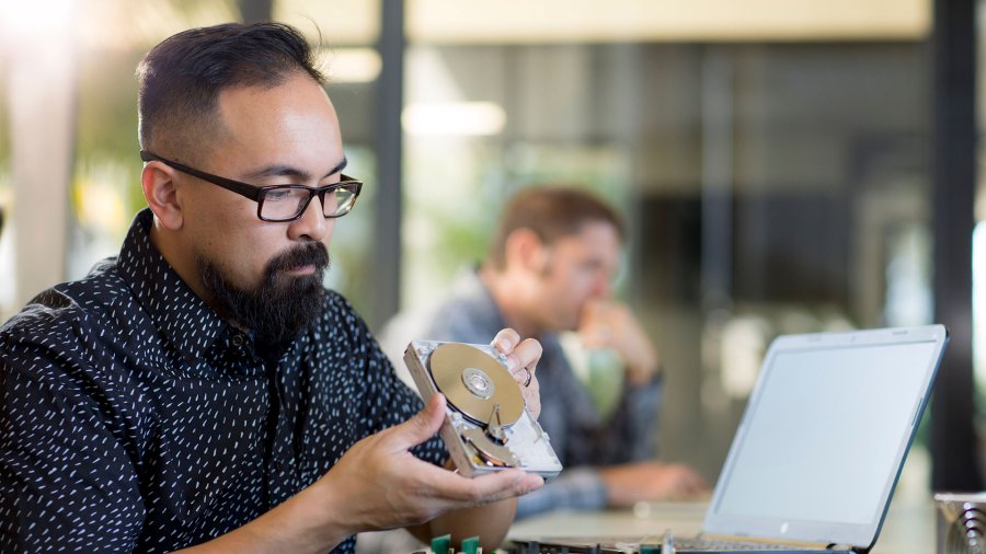 An adult degree student takes apart a computer hard drive and examines it closely.