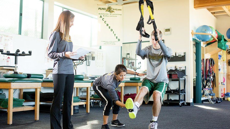 A student trainer helps a PLNU athlete stretch on equipment in the Athletic Training Center.
