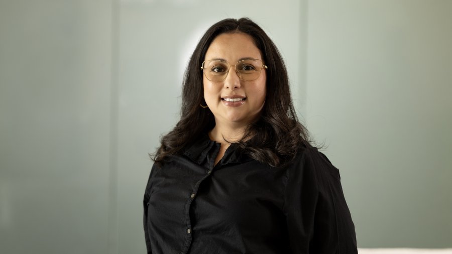 A woman with shoulder-length dark hair and glasses wearing a black blouse poses for a professional portrait.