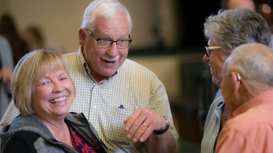 Three gray haired men and an older woman stand together talking and laughing