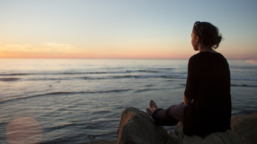 A PLNU student sits on the edge of Sunset Cliffs gazing out on the sunset over the Pacific Ocean