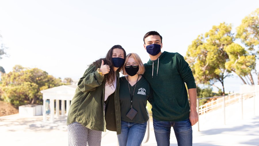 Three masked PLNU students pose for a photo outside