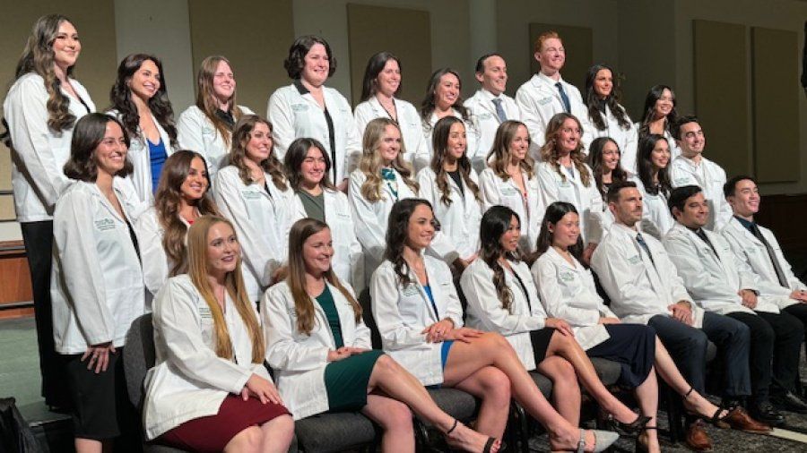 Group of students sit in rows in their white coats 