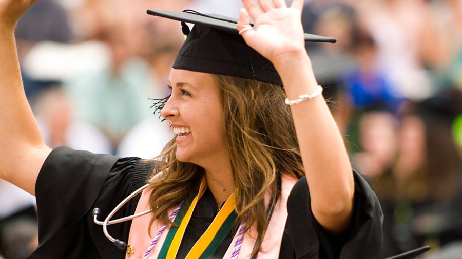 A nursing graduate waves to the crowd at Commencement.
