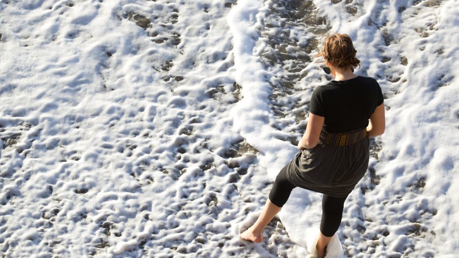 A ariel perspective of a PLNU student walking through the waves on the beach.
