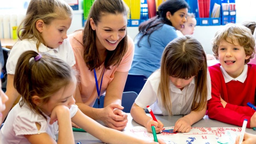 Teacher interacting with preschool aged children as they color around a table 