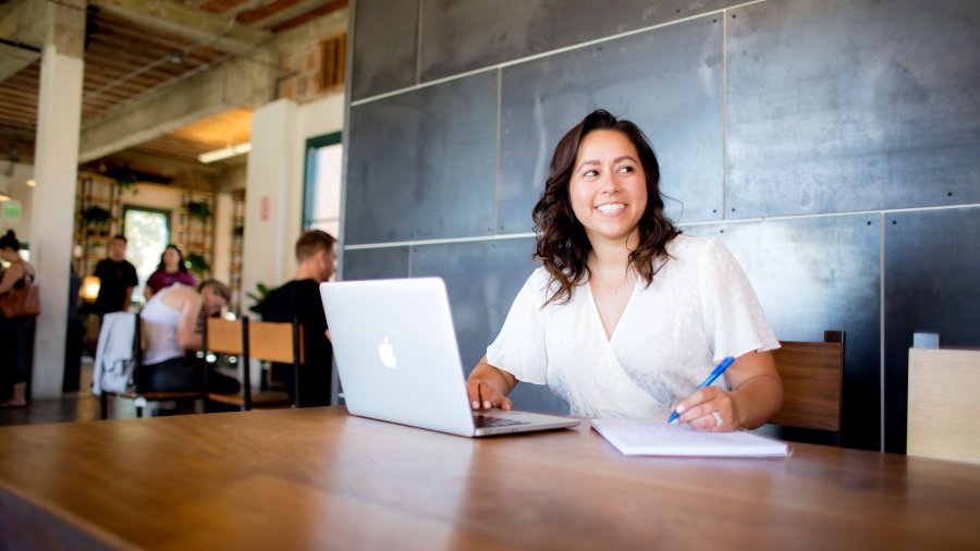 student smiling into the distance as she takes notes for her online class 