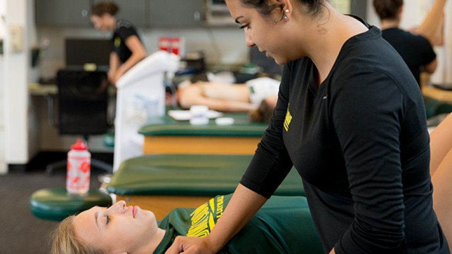 A female trainer helps a PLNU volleyball player stretch before practice.