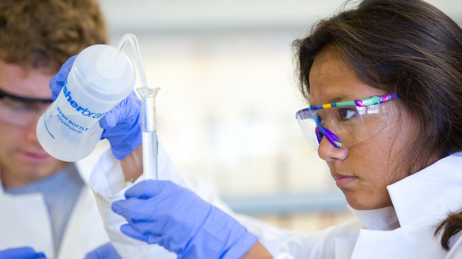 A student is very focused as she pours and measures a liquid for an experiment.