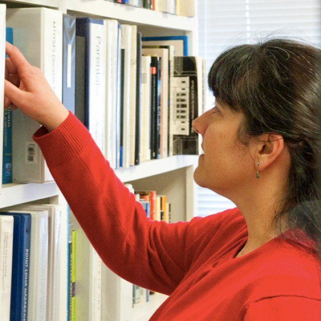 Maria Zack reaches for a book in her office bookcase.