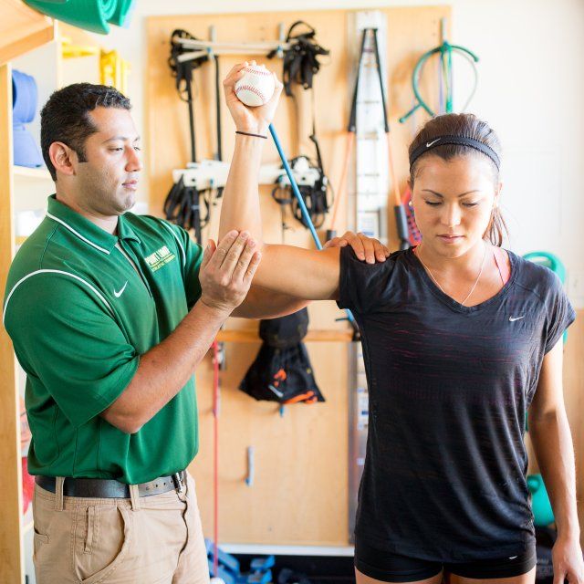 An athletic trainer helps a female athlete stretch her right shoulder