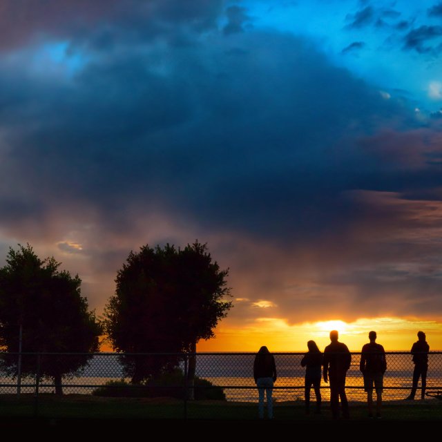 Students stand on the western side of the track and field to watch a sunset