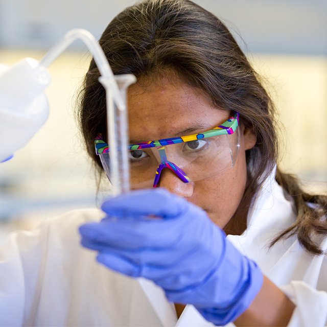 A chemistry student focuses as she pours a liquid into a test tube.