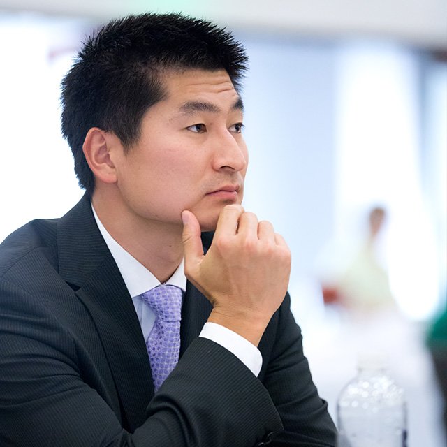 A PLNU graudate student in a black suit with a purple tie focuses on a presentation in class.