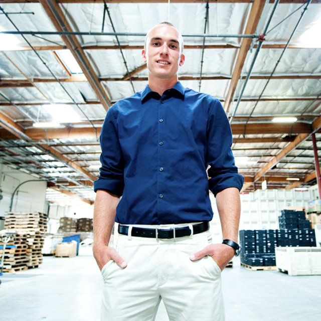 Man in blue shit and white pants standing with his hands in his pockets in a warehouse