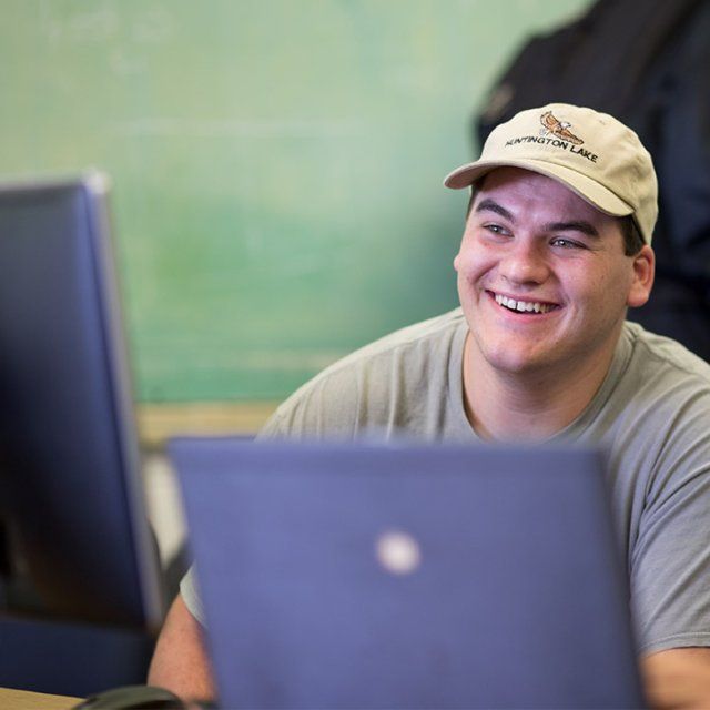 Student smiles while seated behind a computer