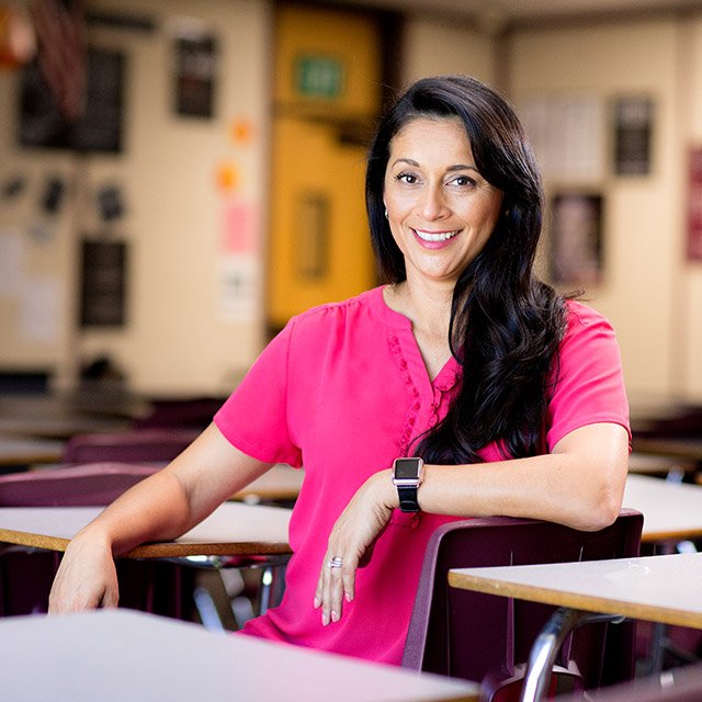 A female teacher sits for a photoshoot in her empty classroom
