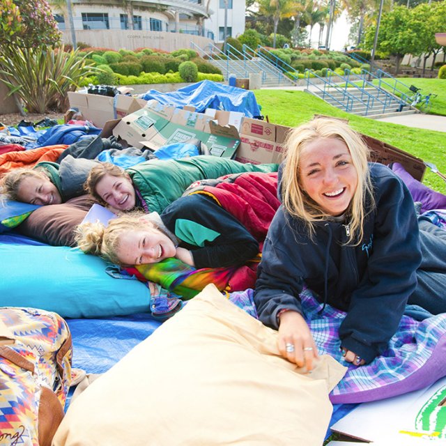 A group of young PLNU women hanging out in sleeping bags on the lawn during two dollar challenge