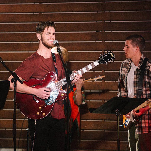 A band of students perform a new song in front of a crowd.