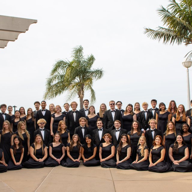 Students in the PLNU choir gather for a group photo on campus with ocean views in the background.