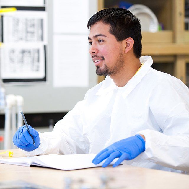 A student wearing a lab coat and safety gloves writes down his observations.