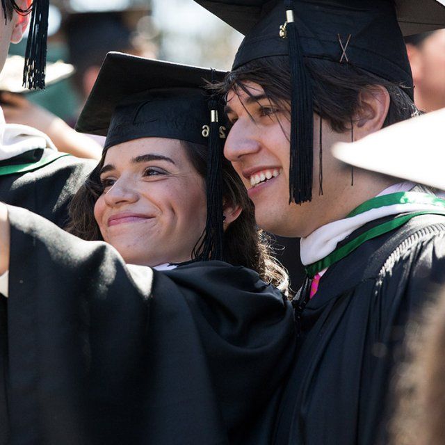 Students at PLNU smiling while taking a selfie at graduation in full cap and gown.