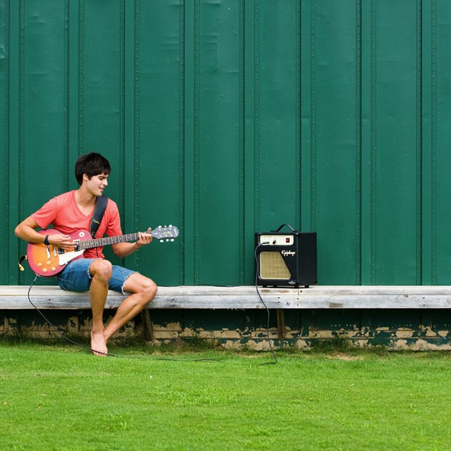 A student plays his guitar outside near the athletic complex
