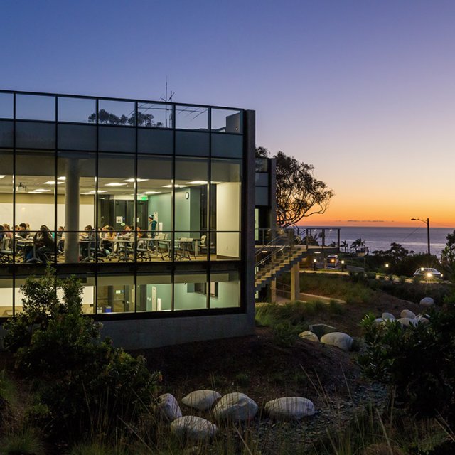 Students attend a night class in Sator Hall with a classic PLNU sunset in the background.