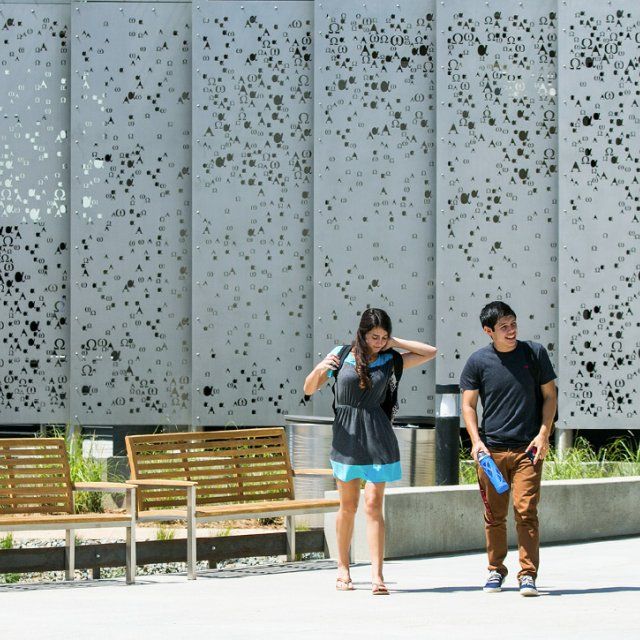 Two students walking down the campus mall with the science building panels behind them