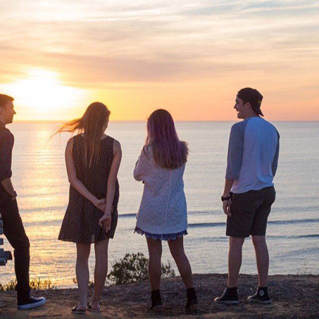 A group of friends watch the sunset over the ocean.