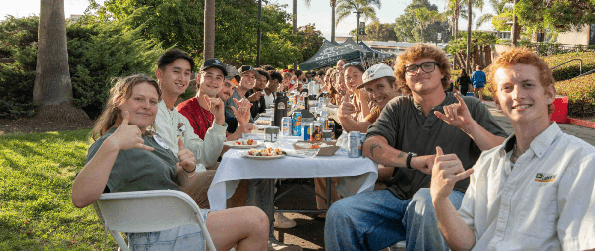 PLNU students smile for a photo on Caf Lane at a banquet dinner table.