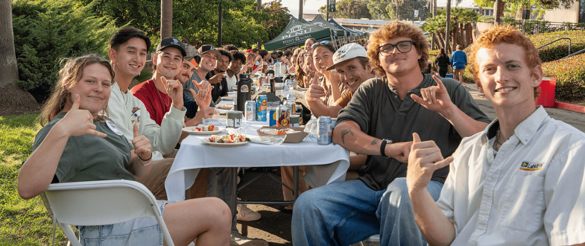 PLNU students smile for a photo on Caf Lane at a banquet dinner table.