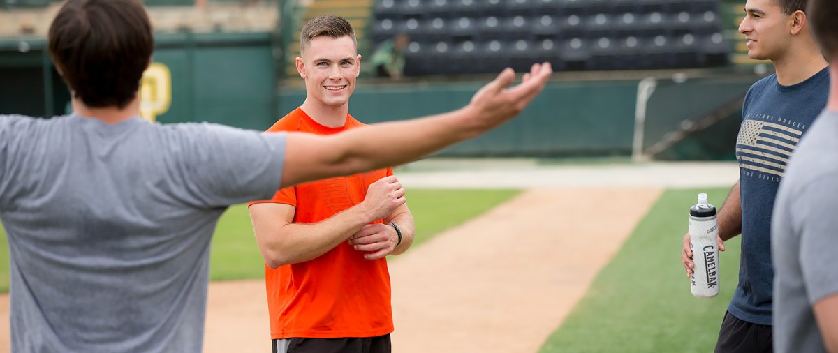 PLNU military students conversing during break at obstacle event on campus baseball field.