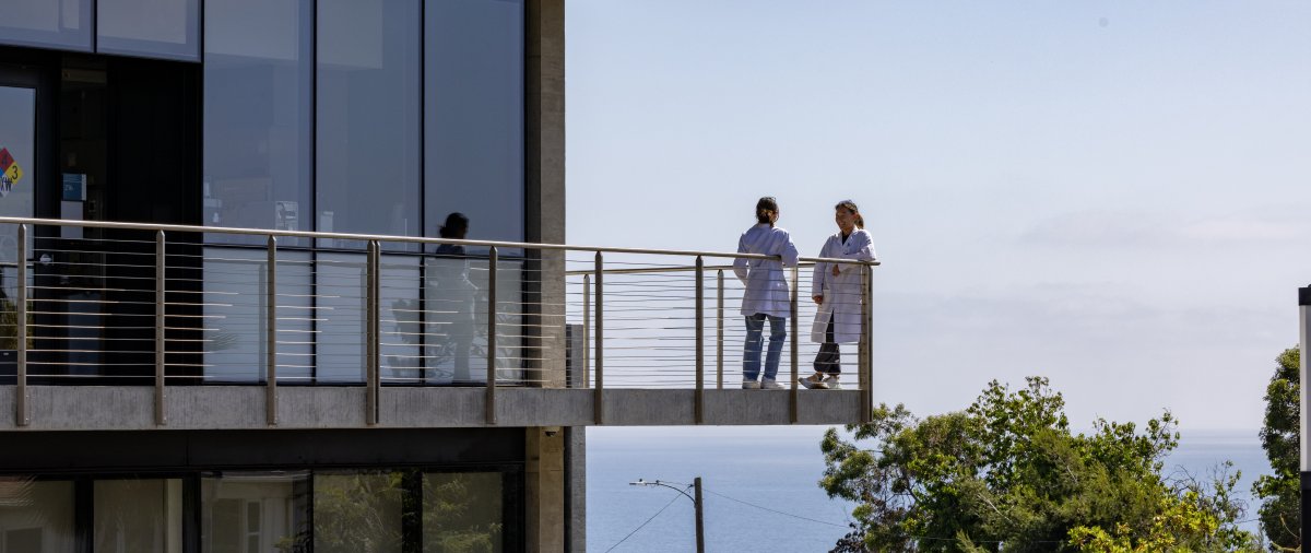 PLNU students standing outside on the balcony of Latter Hall in lab coats.