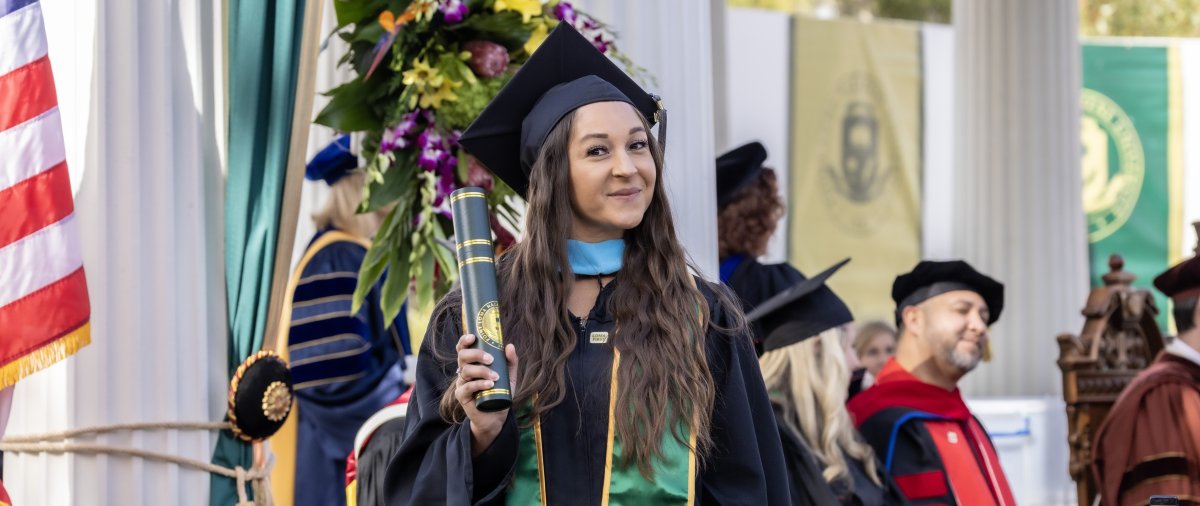 PLNU student posing with degree at commencement ceremony.
