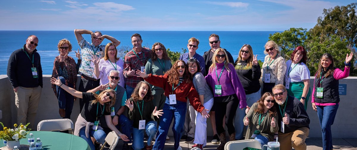 Welcome Week guests smile for a group photo on a campus terrace with ocean views in the background.