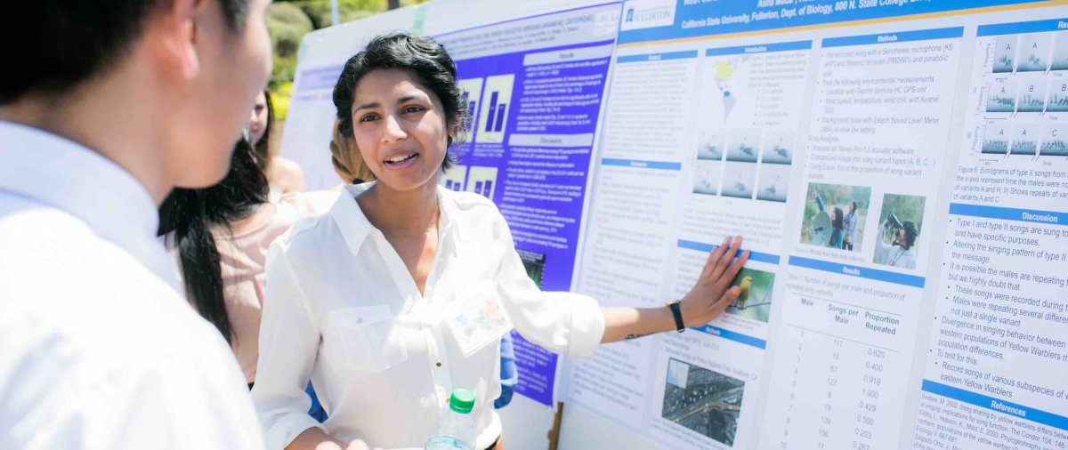 Student researcher discusses her scientific poster with an attendee during an outdoor research presentation.