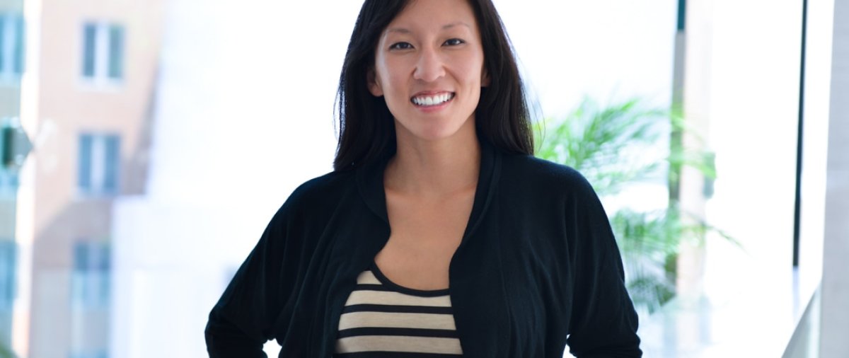 Dr. Kay Tye smiles while standing beside a railing in a bright indoor setting.