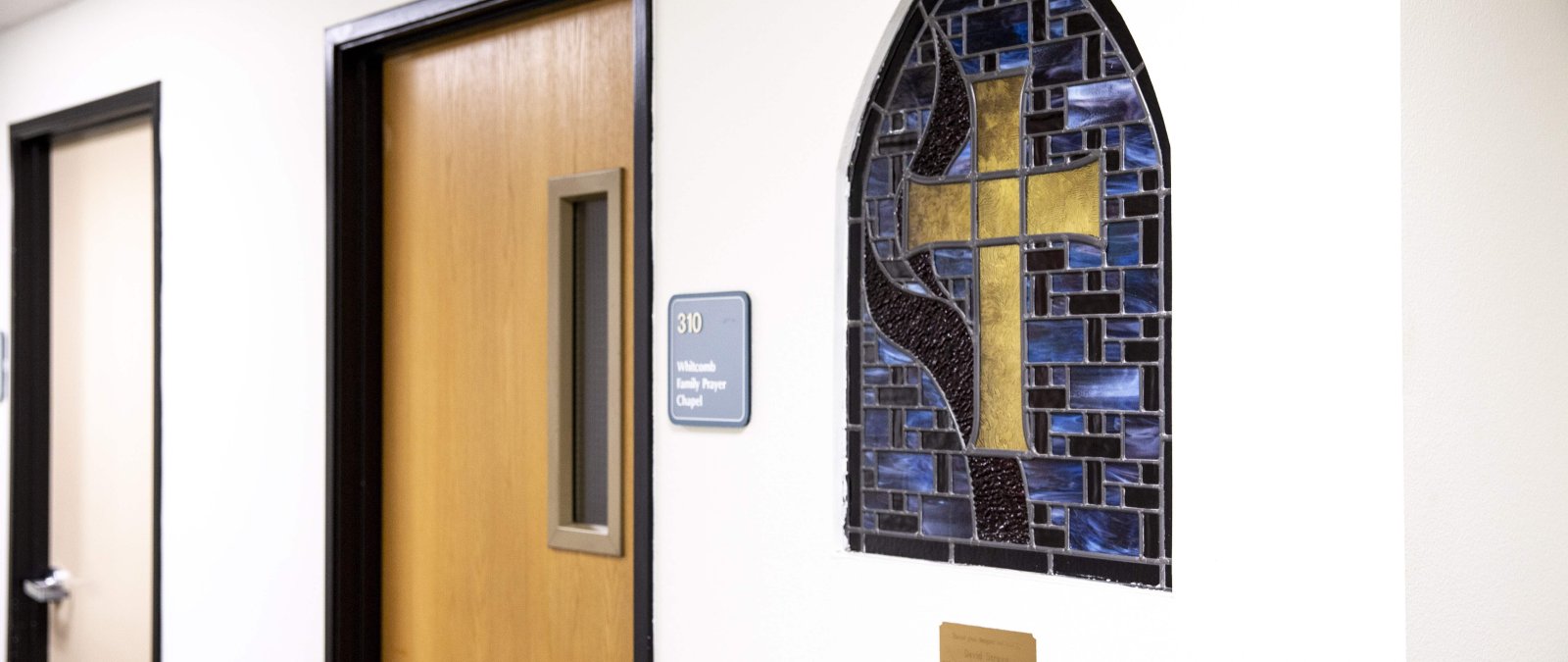 Outside of the chapel room with the door closed. There is a stained glass cross