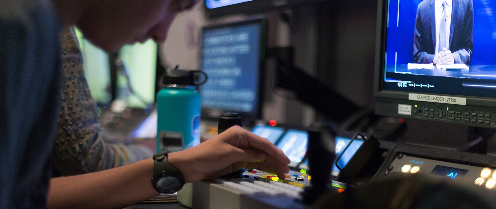 A close up photo of a student pressing buttons on a sound board in the production studio.