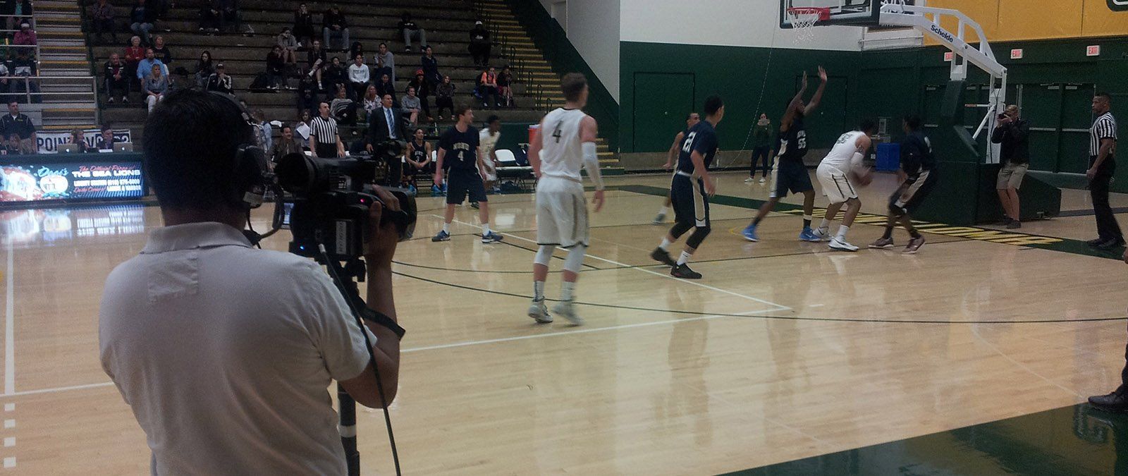 A student films a live broadcast of a men's basketball game.