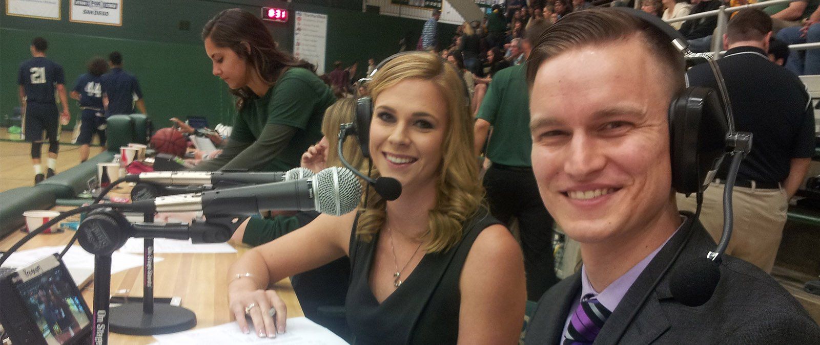 A female and male student broadcasters take in a basketball game.