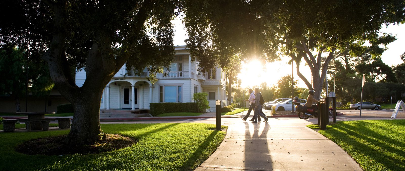 Students walk past Cabrillo Hall with the sun in the background.