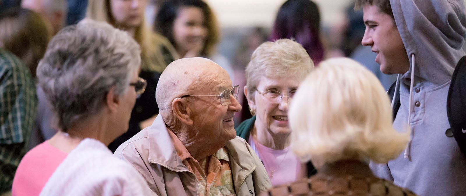 A group of older alumni speak to a current student during a chapel service.