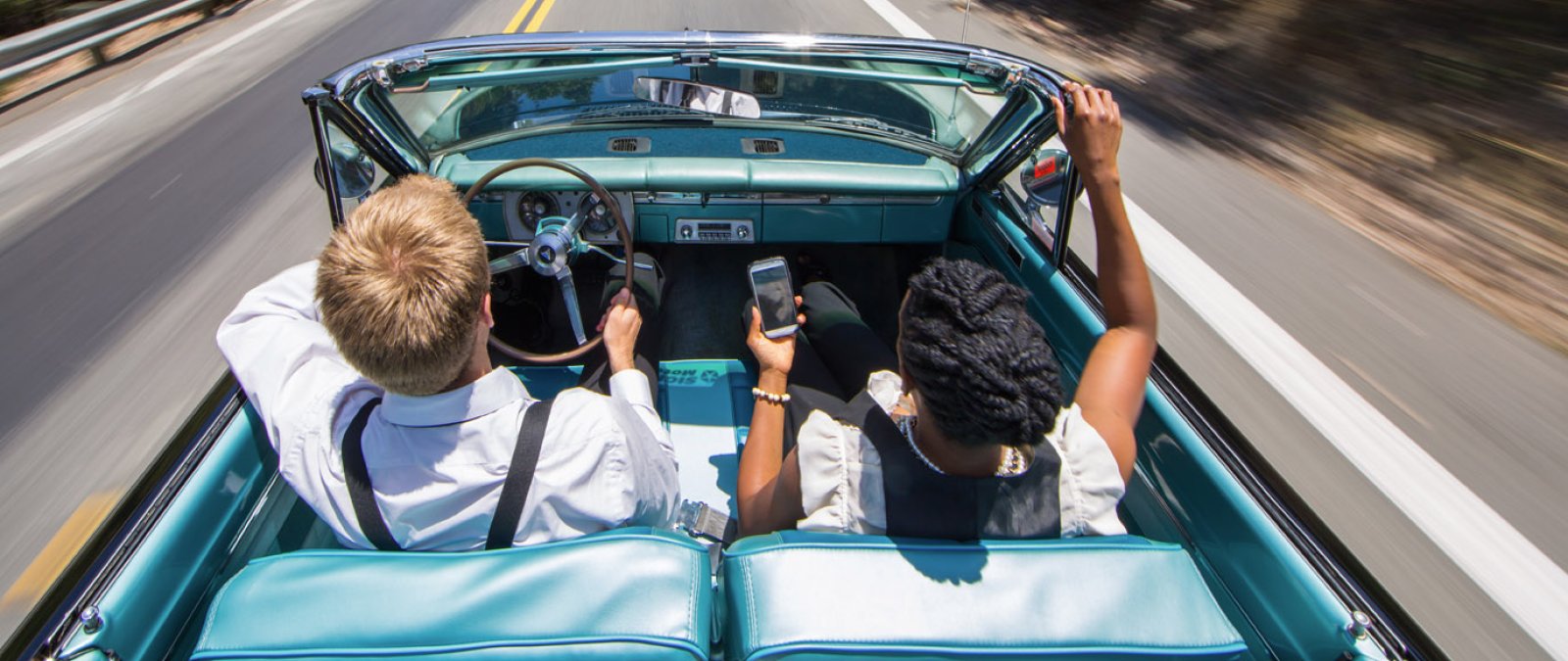 Two students in an old convertible driving fast 