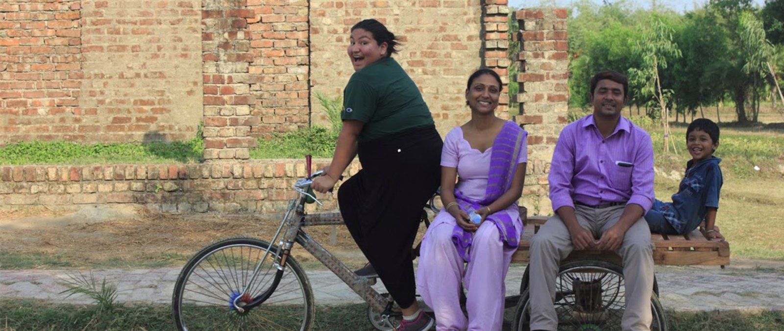 A student pedals a bike carrying a family in India.