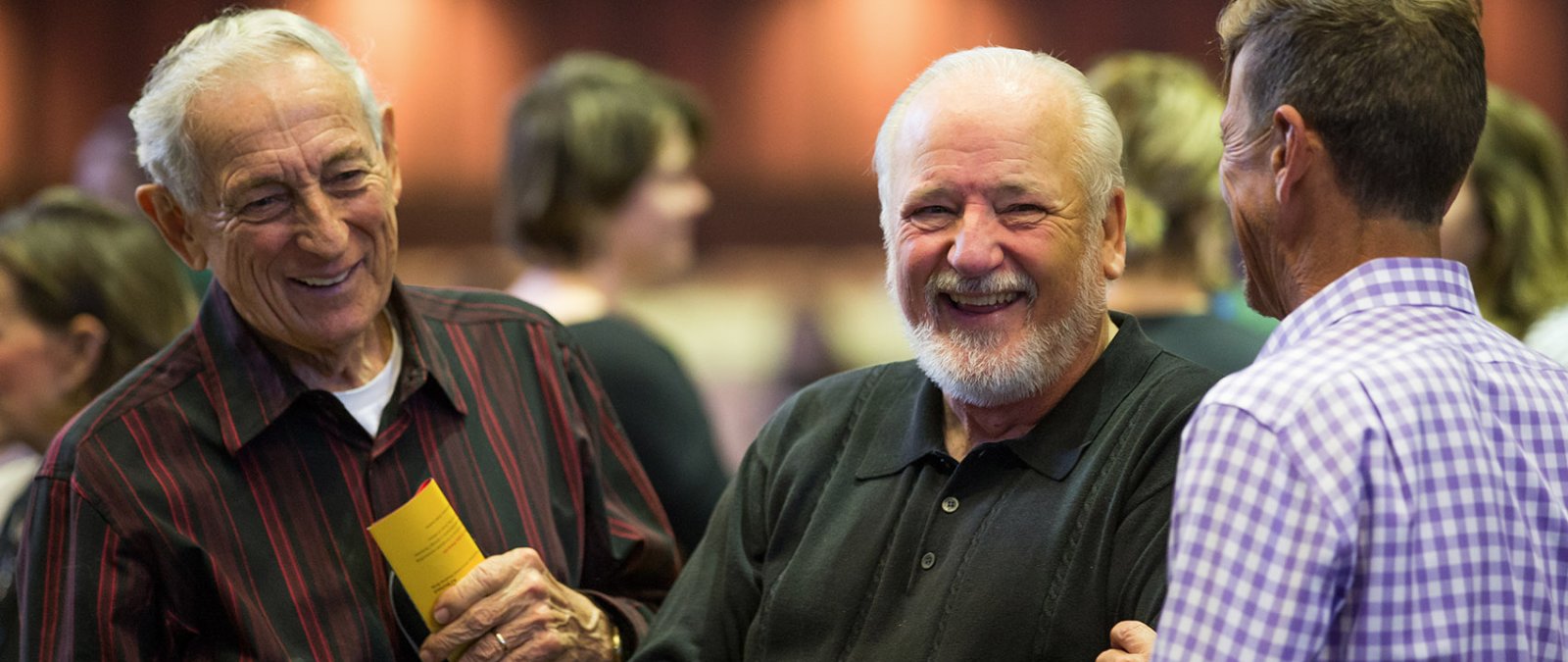 Three older men stand talking and smiling together